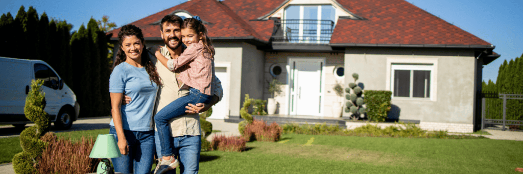 Happy family standing in front of their new home in Tuscarawas County, Ohio—celebrating a successful real estate purchase with the support of local REALTORS®