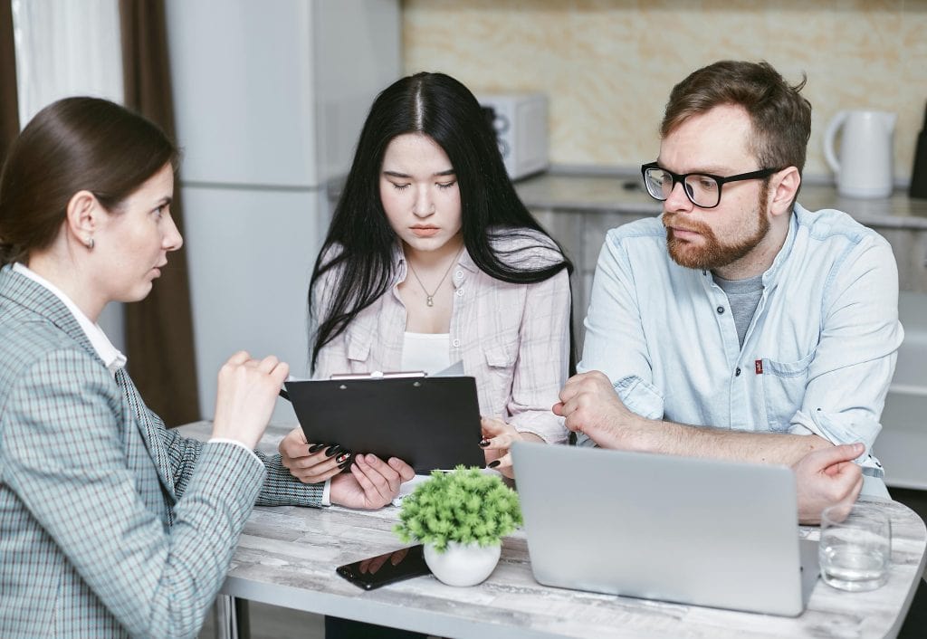 Two adults reviewing mortgage pre-approval details on a tablet while a real estate professional explains the process in Coshocton, Ohio.