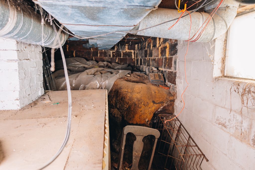 Basement crawl space at 11 Sherman Street, Dennison, Ohio with exposed brick walls, ductwork, and storage items.