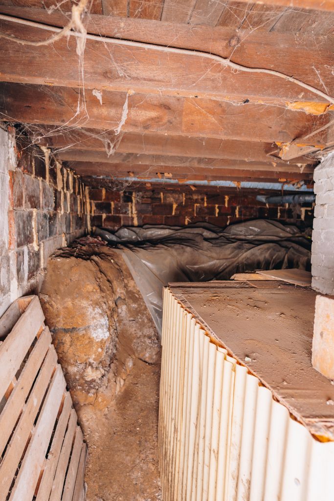 Basement crawl space at 11 Sherman Street, Dennison, Ohio with exposed joists, brick walls, and stored items.