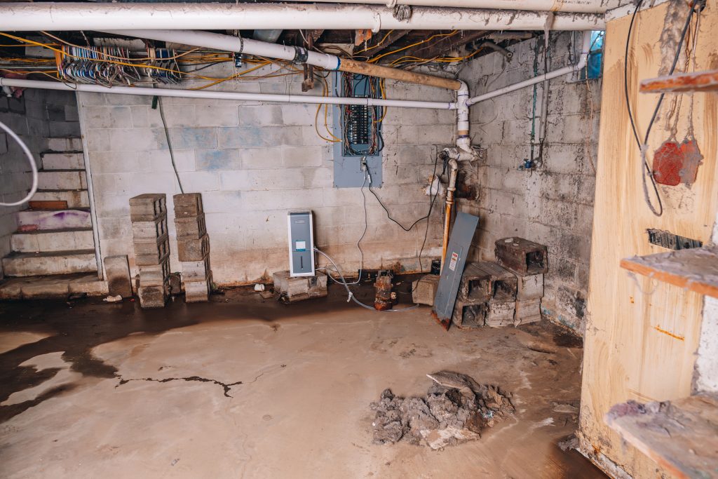 Basement floor at 11 Sherman Street, Dennison, Ohio showing moisture and exposed wiring near electrical panel.Basement floor at 11 Sherman Street, Dennison, Ohio showing moisture and exposed wiring near electrical panel.