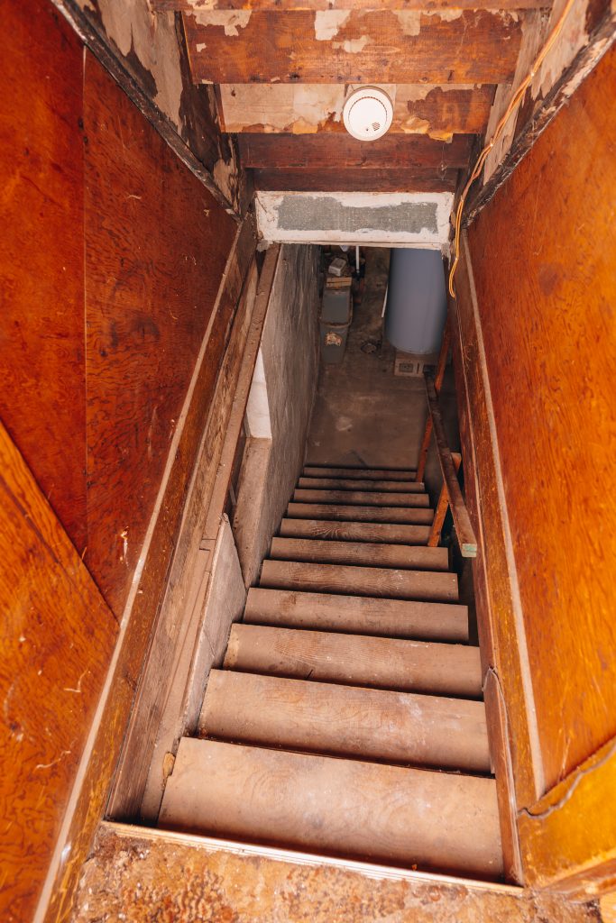 Narrow staircase leading to basement at 11 Sherman Street, Dennison, Ohio with wood paneling and visible water heater