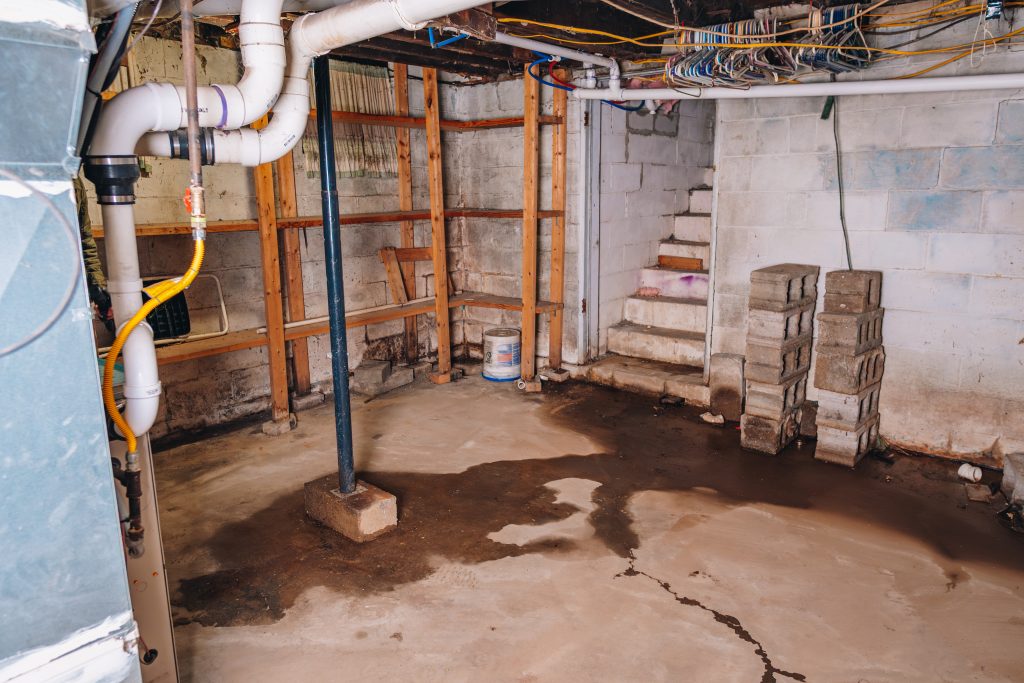 Basement utility area at 11 Sherman Street, Dennison, Ohio with concrete floor, plumbing pipes, and shelving.