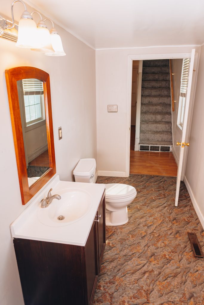 First-floor bathroom at 11 Sherman Street, Dennison, Ohio remodeled in 2022 featuring vanity, toilet, and view of staircase.