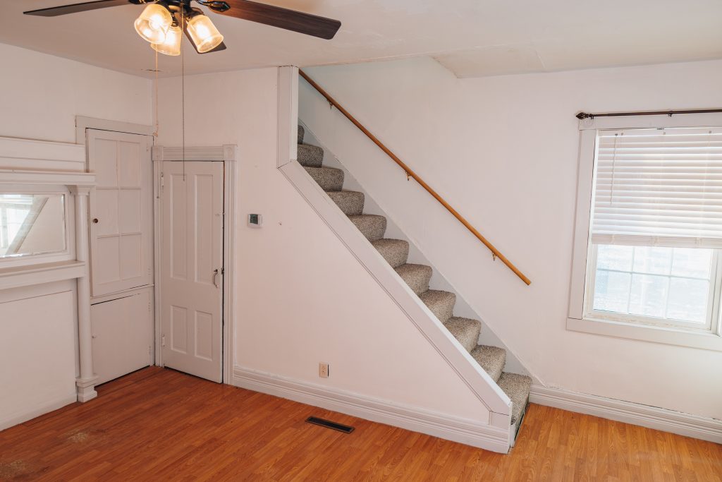 Living and dining room at 11 Sherman Street, Dennison, Ohio with staircase featuring new carpet, ceiling fan, and wood-look flooring.