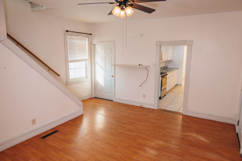 Living room at 11 Sherman Street, Dennison, Ohio featuring staircase with new carpet, ceiling fan, wood-look flooring, and opening to updated kitchen.