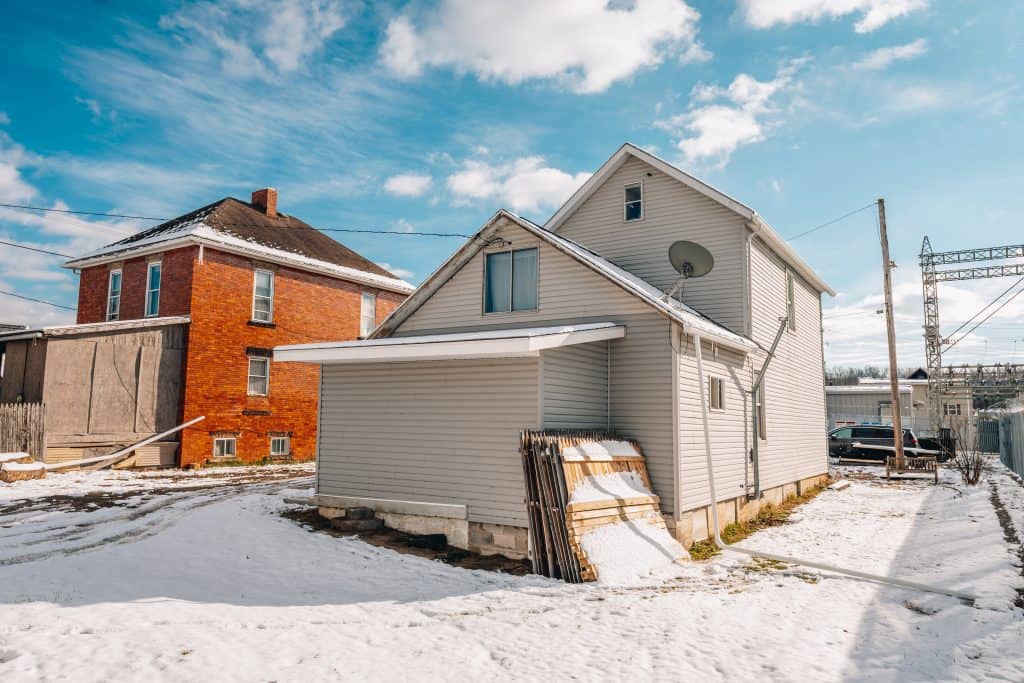 Rear corner view of two-story home at 11 Sherman Street, Dennison, Ohio with beige siding and small entry door. featuring wood fencing
