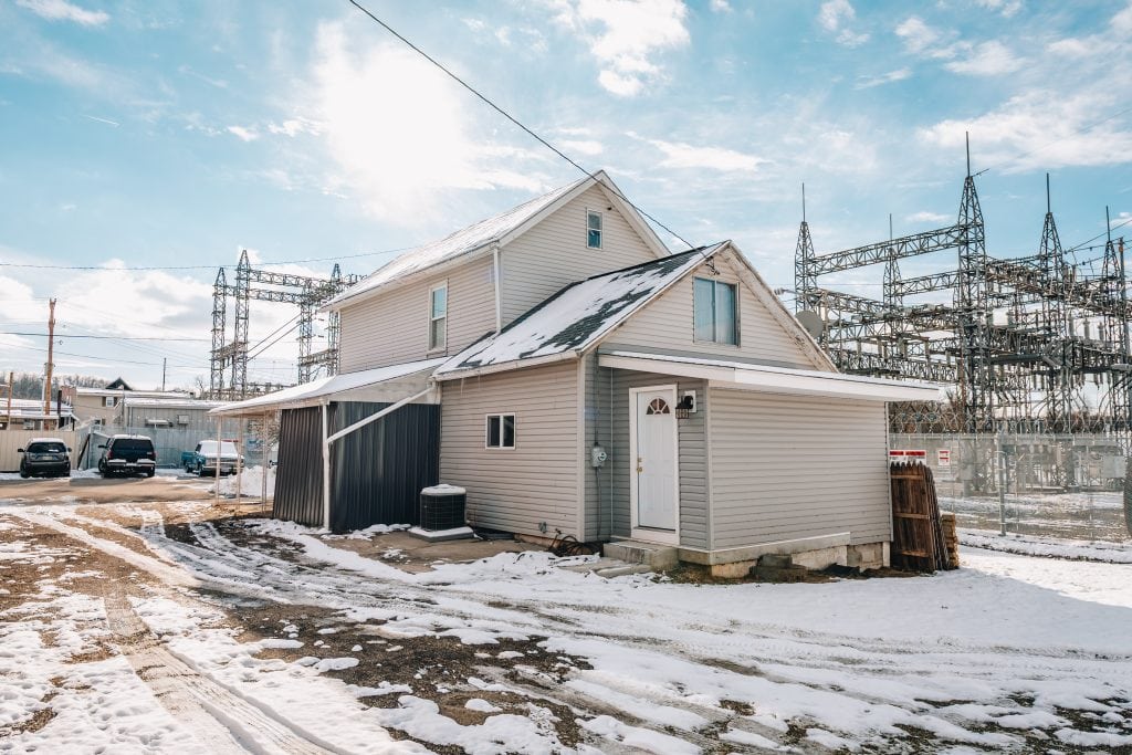Rear corner view of two-story home at 11 Sherman Street, Dennison, Ohio with beige siding and small entry door.