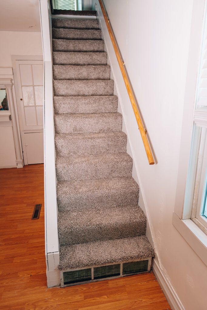 Close-up of staircase at 11 Sherman Street, Dennison, Ohio featuring new carpet and wood handrail.