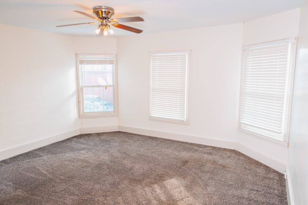 Upstairs bedroom at 11 Sherman Street, Dennison, Ohio with three windows, ceiling fan, and new carpet.