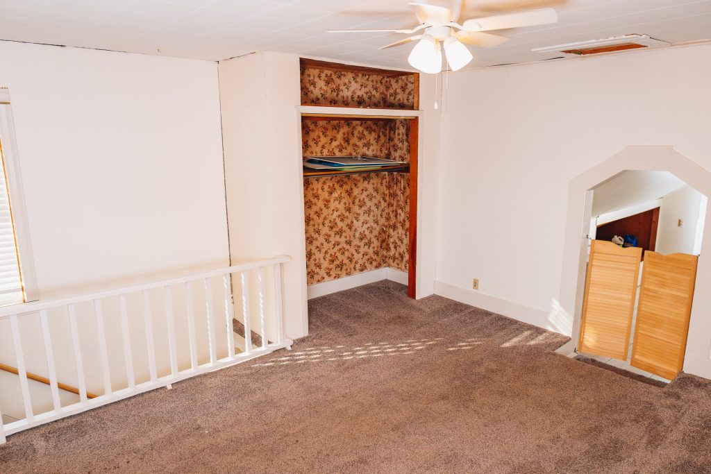 Upstairs bedroom at 11 Sherman Street, Dennison, Ohio featuring open closet with floral lining and archway to adjoining room.
