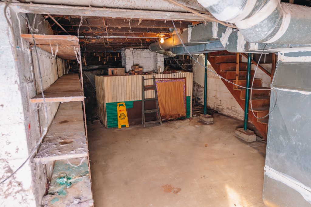 Wide view of basement at 11 Sherman Street, Dennison, Ohio with shelving, ductwork, and concrete floor.